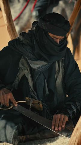 Homme armé enveloppé dans plusieurs tuniques et foulards sombres, lui recouvrant le visage.